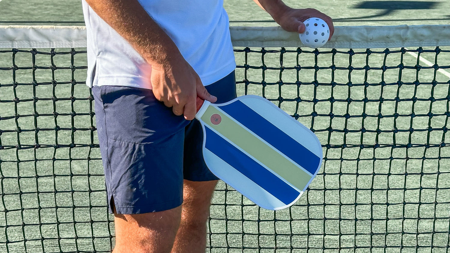 A man standing by a pickleball net holding a fun pickleball paddle