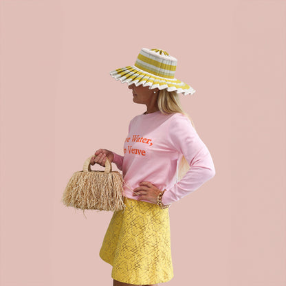 A woman holding a straw bag and wearing a pink sweater with a fun hat